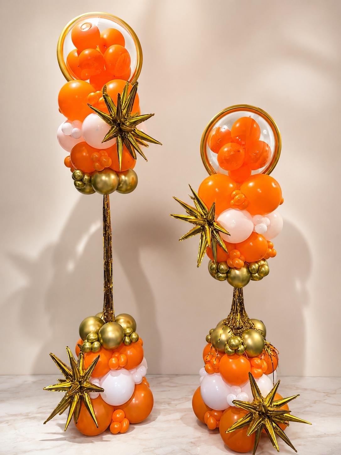 Pair of orange and gold balloon columns with starburst accents