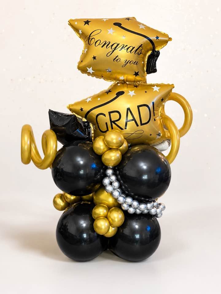Gold Congrats and Grad balloons over a black and gold balloon base