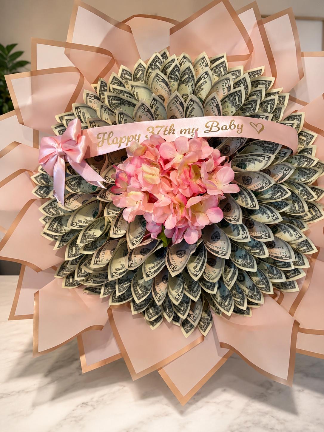 Folded money fan in blush wrapping with a flower center and a banner