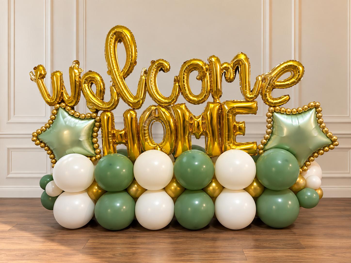 Letras doradas de welcome HOME sobre una base de globos verde salvia y blancos con estrellas verde salvia