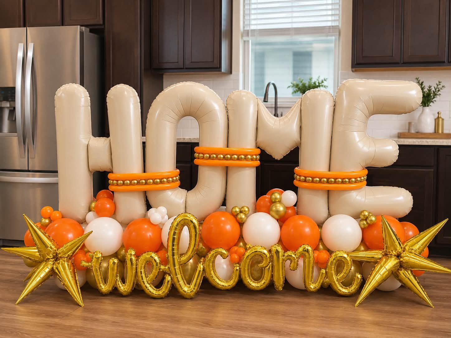 Letras gigantes HOME de globos color crema con la palabra welcome en dorado, globos naranjas y blancos y estrellas doradas